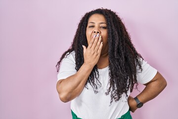 Plus size hispanic woman standing over pink background bored yawning tired covering mouth with...