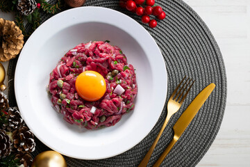 Traditional steak tartare with beef and egg yolk. Christmas food served on a table decorated with Christmas motifs.