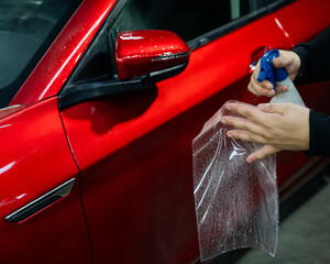 A technician sprays water before applying protective vinyl film to a car.
