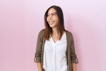 Fototapeta premium Middle age chinese woman wearing glasses over pink background looking away to side with smile on face, natural expression. laughing confident.