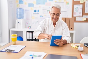 Middle age grey-haired man business worker smiling confident using touchpad at office