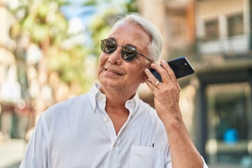 Middle age grey-haired man smiling confident listening audio message by the smartphone at street