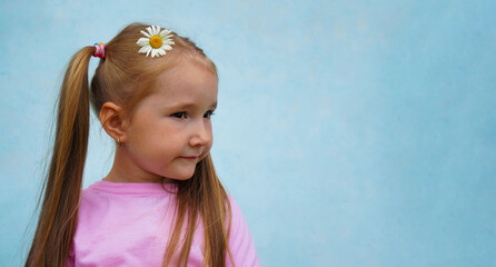 Positive girl. Little girl with daisies on a blue background. The child holds flowers and mysteriously smiles. Greeting Card.