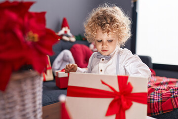 Fototapeta na wymiar Adorable blond toddler unpacking christmas gift standing at home