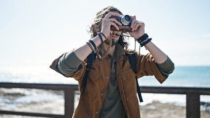 Young hispanic man tourist wearing backpack make photo at seaside