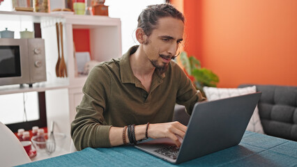 Young hispanic man using laptop sitting on table at dinning room