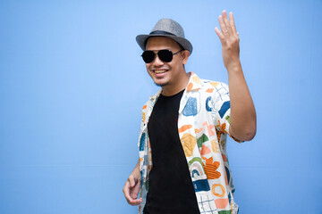 Fototapeta premium asian man wearing beach shirt pointing a finger to vacation discount offer. Isolated on blue background. Vacation concept