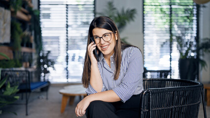 Young beautiful hispanic woman speaking on the phone sitting on a chair at the office