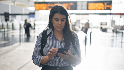 Young beautiful hispanic woman walking down the railway using smartphone at train station