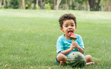 Portrait of little african curly hair cute boy playing, openning large mouth to eat piece of...