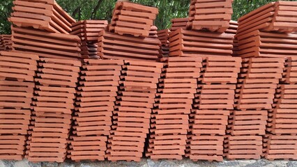 A load of rectangular shaped red clay roofing tiles stacked on a stone ledge by construction workers, unintentionally creating a beautiful pattern and a unique background and texture.  