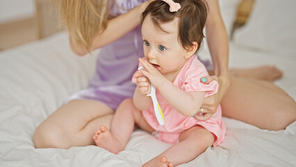 Mother and daughter sitting on bed combing hair at bedroom