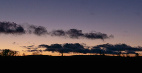 Sunset over the ridge with silhouette of trees under the dark clouds. Dramatic landscape.