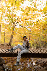 Fototapeta premium Woman with mobile phone and headphones in forest wearing yellow hat, listening to music, taking photos and video call