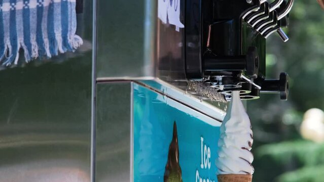 Close-up of female seller making soft serve ice cream from machine outdoors. Takeaway food and summer season concept