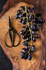on a rough wooden board, a bunch of black grapes and a pair of scissors