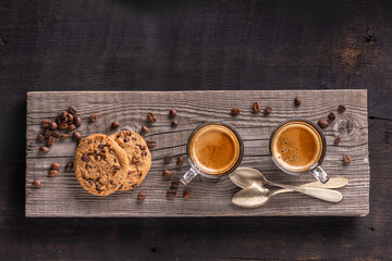 On the rustic wooden table, in the foreground, two fragrant coffees in glass cups, and chocolate chip cookies - 685824580