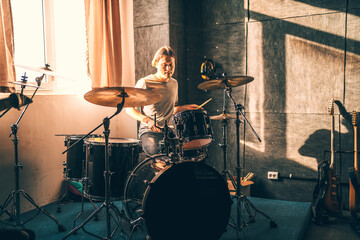 Drummer plays drums in music studio at band rehearsal. Musician with instrument in beautiful sunset light from window.