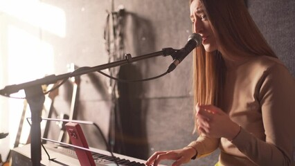 Beautiful musician woman sings and plays synthesizer at rehearsal for performance with her music band in recording studio. Voice training and teaching by professional artist singer. - Powered by Adobe