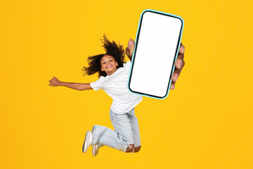 African teenage girl showing huge smartphone blank screen leaping, studio