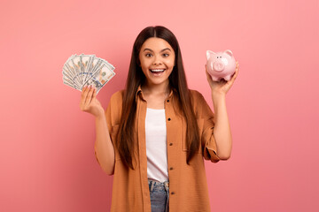 Joyful teen girl holding piggy bank in hand and fan of cash