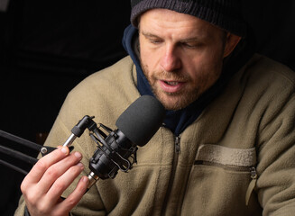 White man speaking to a microphone isolated on dark background, hipster look