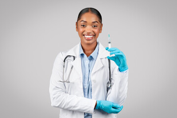 Happy pretty young black lady doctor in white coat show syringe, recommends injection, health care