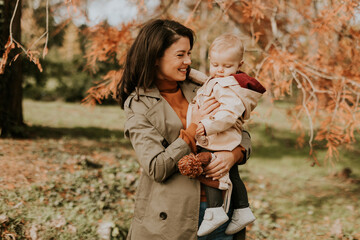 Young woman holding cute baby girl in the autumn park