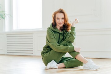 Radiant woman in a cozy green tracksuit sitting on the floor, relaxed home setting with natural light, fresh and comfortable