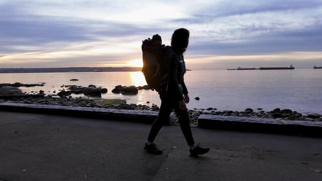 Mother with Baby in Carrier on Seawall in Stanley Park. Sunset, Fall Season. Downtown Vancouver, British Columbia, Canada.