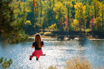 A young girl on an extreme swing over a cliff at the top of a mountain in autumn with a view of the...