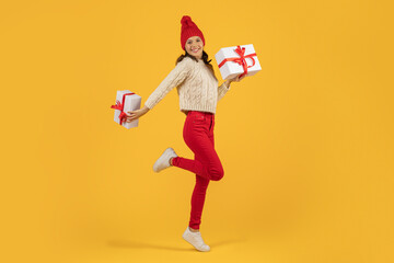 Fototapeta na wymiar Joyful woman jumping with Xmas holiday presents on yellow backdrop