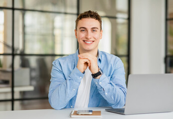 Positive handsome young european man manager in casual with laptop at table