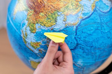 A man holds a paper airplane poised over a globe, embodying the spirit of adventure and travel