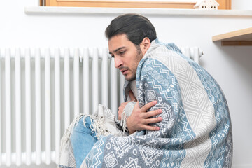 Man freezing at home and sitting by the radiator. Freezing guy warming close to heating system....