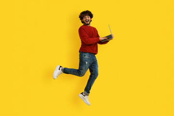 Emotional indian man enjoying great online offer, jumping with laptop