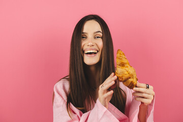 Brunette happy woman having a relaxing moment hold croissant and eat it. Attractive caucasian girl...