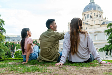 Relaxed trio sits on grass overlooking historic dome, sharing stories in the warmth of a sunny day