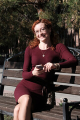 A European woman with red hair sits talking on a smartphone. Background park. Concept of negotiations, communication on the phone.