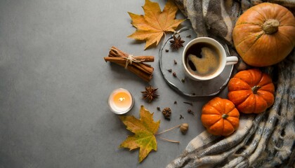 coziness of being at home in autumn above view photo of a cup of hot coffee patchy blanket pumpkin shaped candles maple foliage and aromatic spices on grey background with copy space