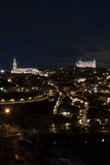 Fototapeta na wymiar Historic center of Toledo, Spain, at night with the light of street lamps and the cathedral of Santa María and the Royal Alcázar (army museum today) illuminated. UNESCO World Heritage Site