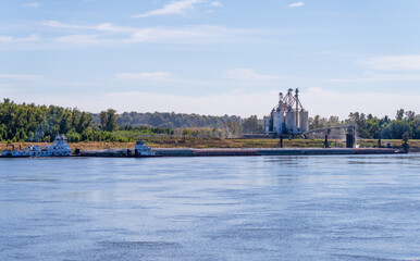 Fototapeta premium Tugboat pushing freight barges past grain loading dock in farming country in Kentucky
