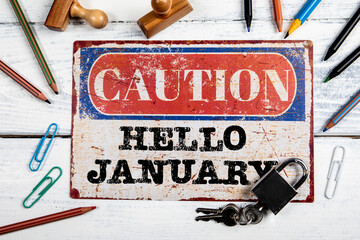 Hello January. Metal CAOTION plate with text on a white wooden background