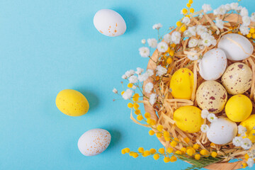 Easter candy chocolate eggs and almond sweets lying in a bird's nest decorated with flowers and feathers on a blue background. Happy Easter concept.