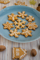 Painted traditional Christmas gingerbreads arranged on blue plate on white wooden table, various xmas shapes