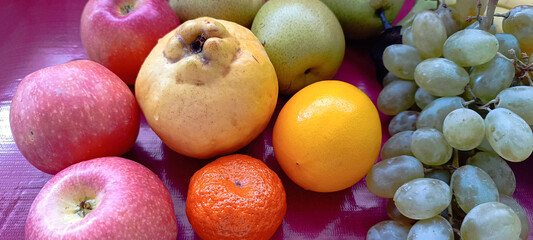 A bunch of ripe fruits, apples, quince, tangerine, pears, grapes on a purple background