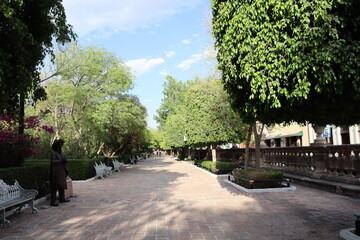 Traditional public garden, park with benches and bronze statues, alley in the park.