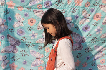 Niña de ocho años en las afuera iluminada con la luz del sol de tarde enfrente de una tela con textura con detalles de flores y mariposas