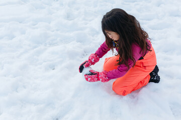 upper view on girl with long hair sitting on snow making snow ball
