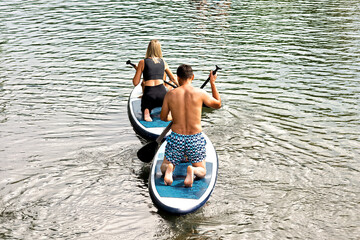 A man and woman sup surfing paddling on a boat on the river in summer.